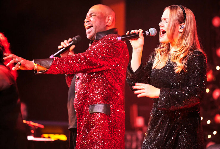 Zwei Sänger in glitzernden Outfits performen leidenschaftlich auf einer Bühne.