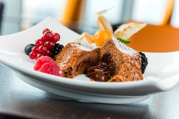 Schokoladenfondant mit flüssigem Kern, dekoriert mit frischen Beeren und Physalis auf einem weißen Teller.
