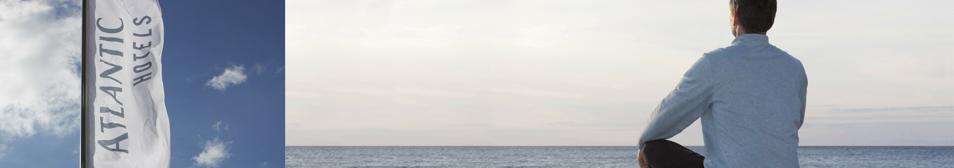 Eine Flagge mit „Atlantic Hotels“ weht im Wind; daneben sitzt eine Person am Meer und blickt auf den Horizont.