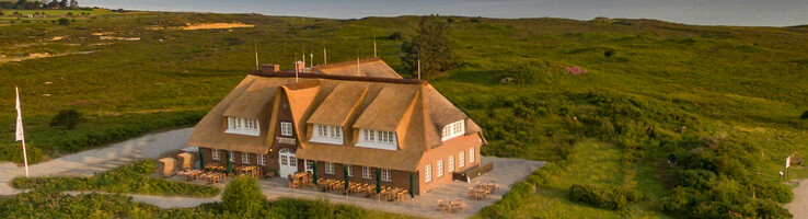 Landhaus Severin*s Morsum Kliff auf Sylt Reetgedecktes Hotel in grüner Landschaft am Meer, mit Terrasse und umliegenden Wegen.