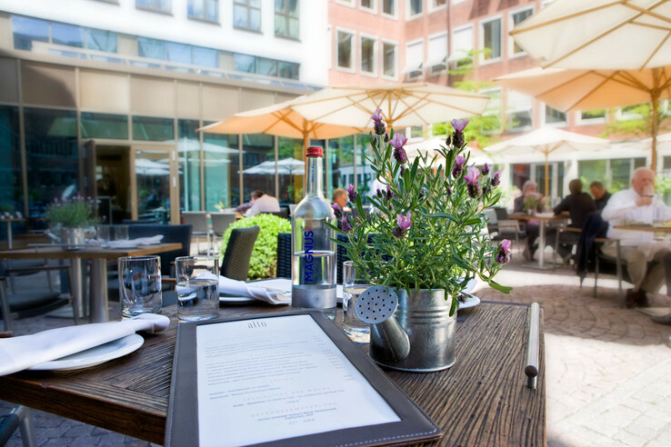 Outdoor terrace of the ATLANTIC Grand Hotel Bremen with laid table, menu, lavender in a watering can and parasols.
