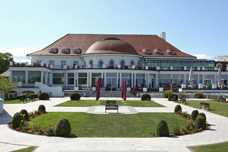 Das ATLANTIC Grand Hotel Travemünde mit gepflegtem Garten und roten Sonnenschirmen vor der eleganten Fassade.