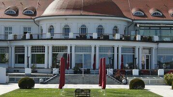 Das ATLANTIC Grand Hotel Travemünde mit gepflegtem Garten und roten Sonnenschirmen vor der eleganten Fassade.
