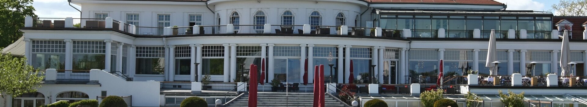 ATLANTIC Grand Hotel Travemünde Außenansicht mit Parkanlage Das ATLANTIC Grand Hotel Travemünde mit gepflegtem Garten und roten Sonnenschirmen vor der eleganten Fassade.