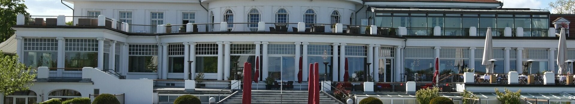 ATLANTIC Grand Hotel Travemünde Außenansicht mit Parkanlage Das ATLANTIC Grand Hotel Travemünde mit gepflegtem Garten und roten Sonnenschirmen vor der eleganten Fassade.