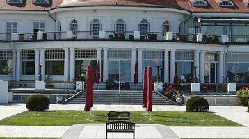 Das ATLANTIC Grand Hotel Travemünde mit gepflegtem Garten und roten Sonnenschirmen vor der eleganten Fassade.