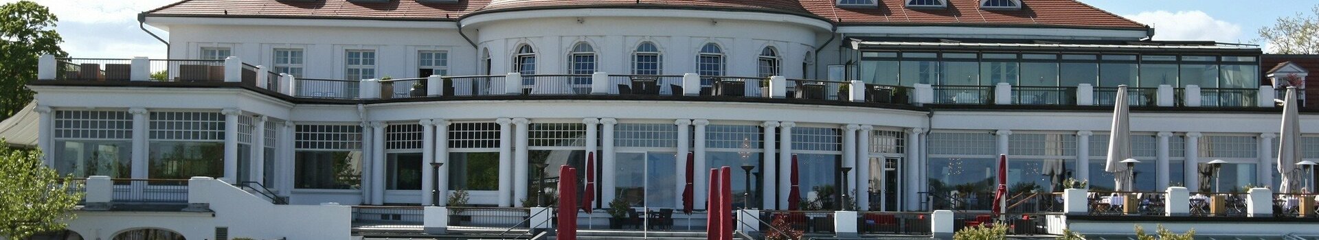 ATLANTIC Grand Hotel Travemünde Außenansicht mit Parkanlage Das ATLANTIC Grand Hotel Travemünde mit gepflegtem Garten und roten Sonnenschirmen vor der eleganten Fassade.