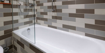 Modern bathroom bathtub with glass partition, surrounded by stylish beige-grey tiles in the ATLANTIC Hotel Galopprennbahn.