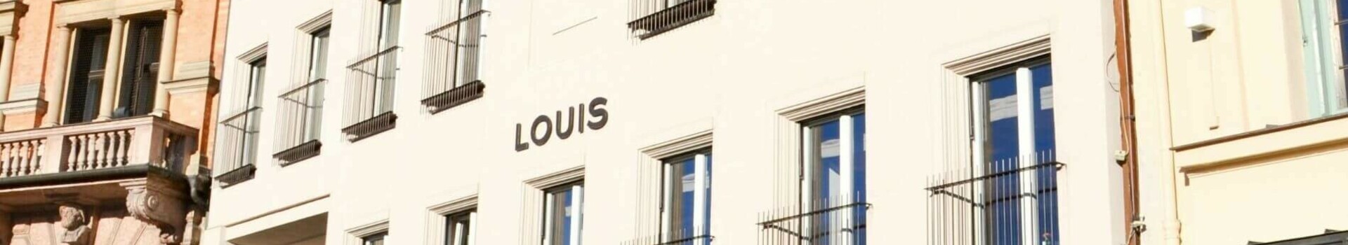 LOUIS Hotel München Façade of a hotel with many windows and the lettering "LOUIS" in a historic building environment.