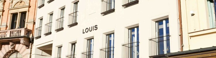 LOUIS Hotel München Fassade eines Hotels mit vielen Fenstern und dem Schriftzug "LOUIS" in einem historischen Gebäudeumfeld.