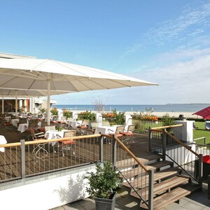 Hotelterrasse mit Tischen und Stühlen, Blick auf die Ostsee, Sonnenschirme, gepflegter Garten mit Strandkörben.
