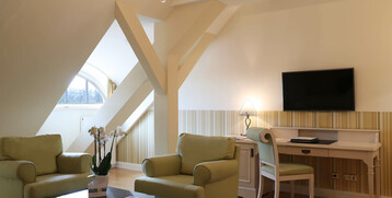 Comfortable hotel suite with pastel-colored armchairs, desk, flat-screen TV and decorative chandelier.
