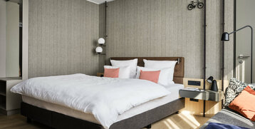 Modernes Hotelzimmer mit Doppelbett, stilvoller Beleuchtung, eleganter Tapete und dekorativen Fahrradmotiven an der Wand.