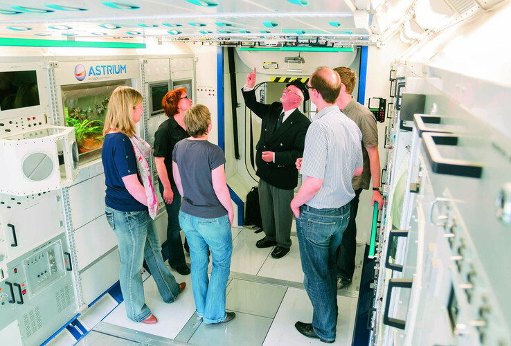A group of people in a modern room with technical equipment, a man explains something.