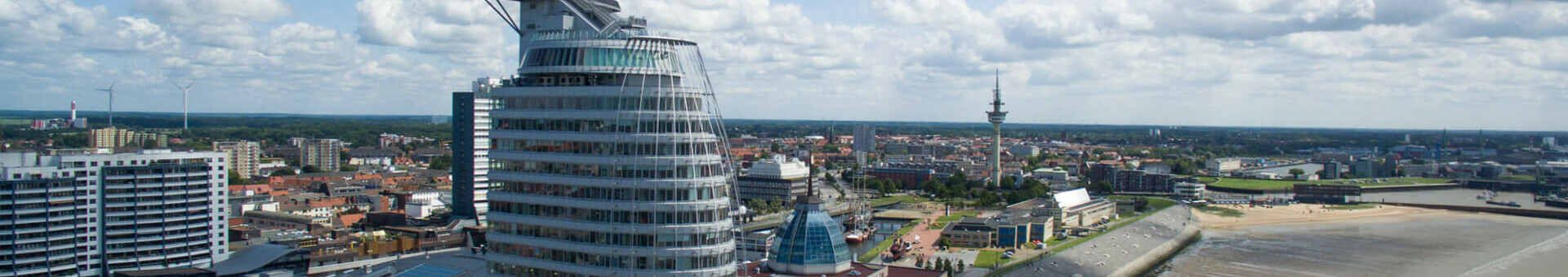 ATLANTIC Hotel Sail City in Bremerhaven, modern high-rise building on the waterfront with a view of the city and coast under a blue sky.