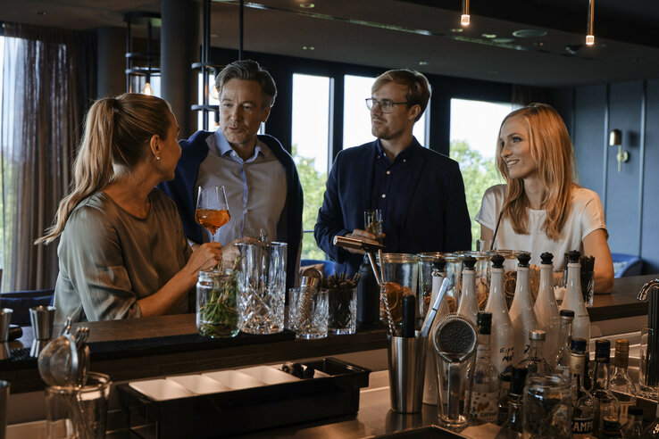 Four people chatting happily at a stylish hotel bar with drinks at the ATLANTIC Hotel Münster.