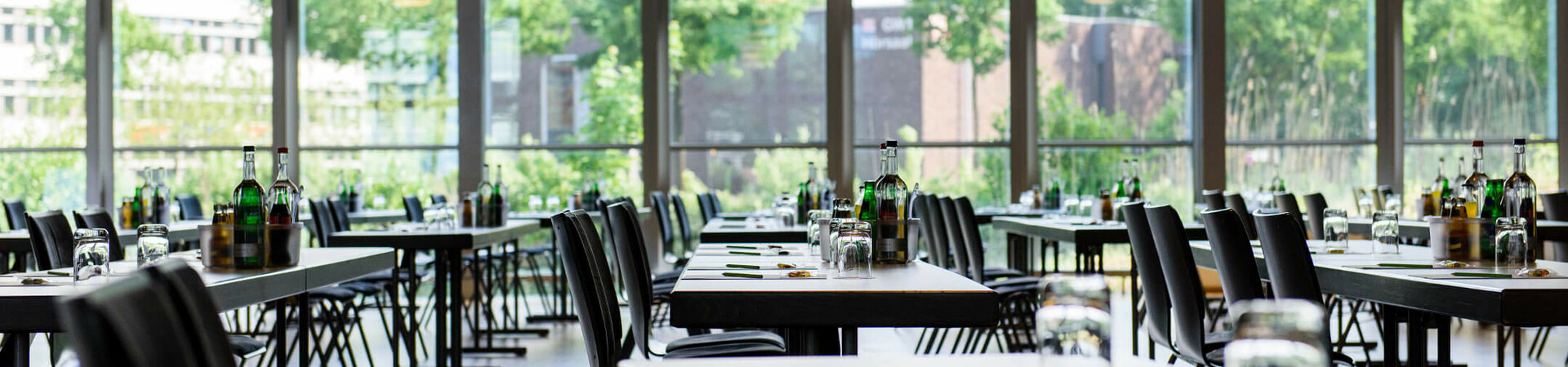 Heller, moderner Konferenzraum mit großen Fenstern, gedeckten Tischen und Blick ins Grüne im ATLANTIC Hotel Universum.