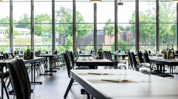 Heller, moderner Konferenzraum mit großen Fenstern, gedeckten Tischen und Blick ins Grüne im ATLANTIC Hotel Universum.