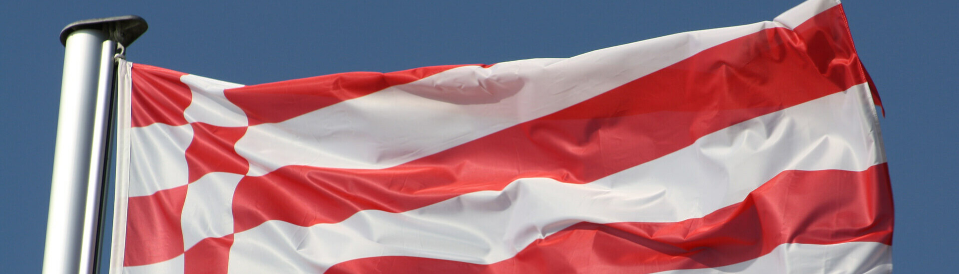 Red and white flags waving in the wind against a clear blue sky.
