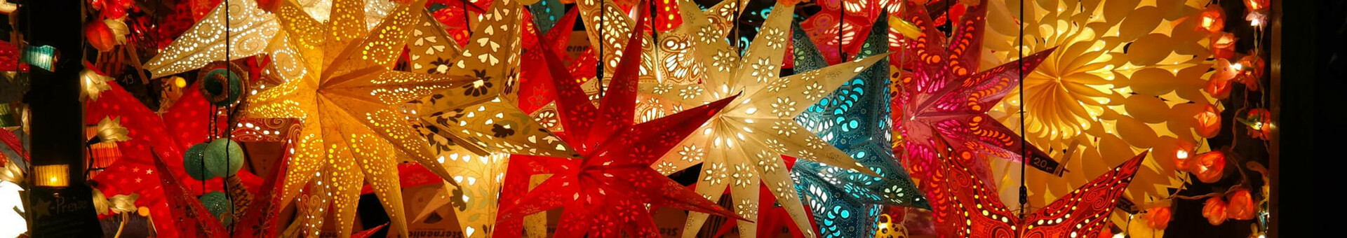 Bunte, leuchtende Papiersterne und Lichterketten schmücken einen festlichen Marktstand bei Nacht.