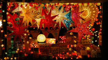 Bunte, leuchtende Papiersterne und Lichterketten schmücken einen festlichen Marktstand bei Nacht.