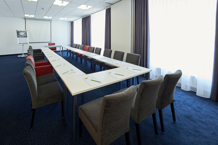 Konferenzraum mit U-förmiger Tischanordnung, grauen Stühlen, Flipchart und Leinwand im ATLANTIC Hotel Vegesack.