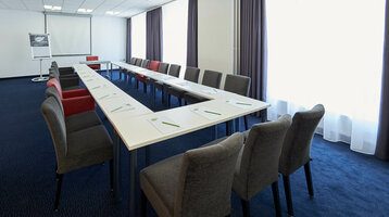 Konferenzraum mit U-förmiger Tischanordnung, grauen Stühlen, Flipchart und Leinwand im ATLANTIC Hotel Vegesack.