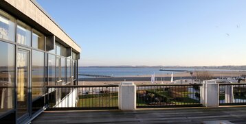 Blick von der Terrasse des ATLANTIC Grand Hotel Travemünde auf Strand, Meer und Promenade bei klarem Himmel.