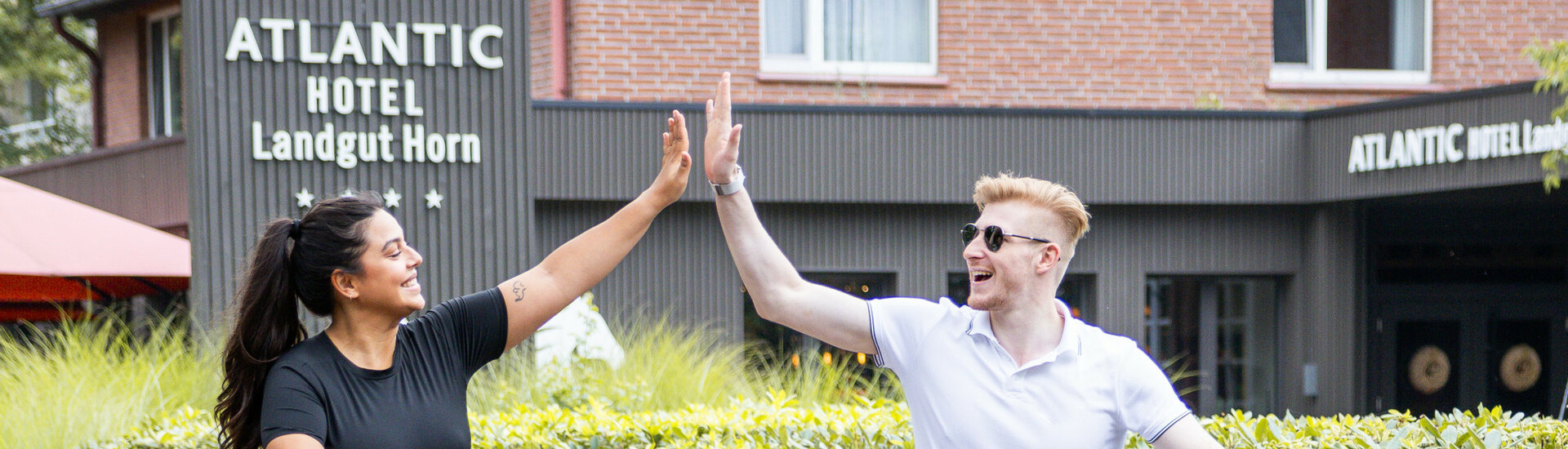 Ein Paar klatscht sich fröhlich auf dem Fahrrad ab vor dem ATLANTIC Hotel Landgut Horn