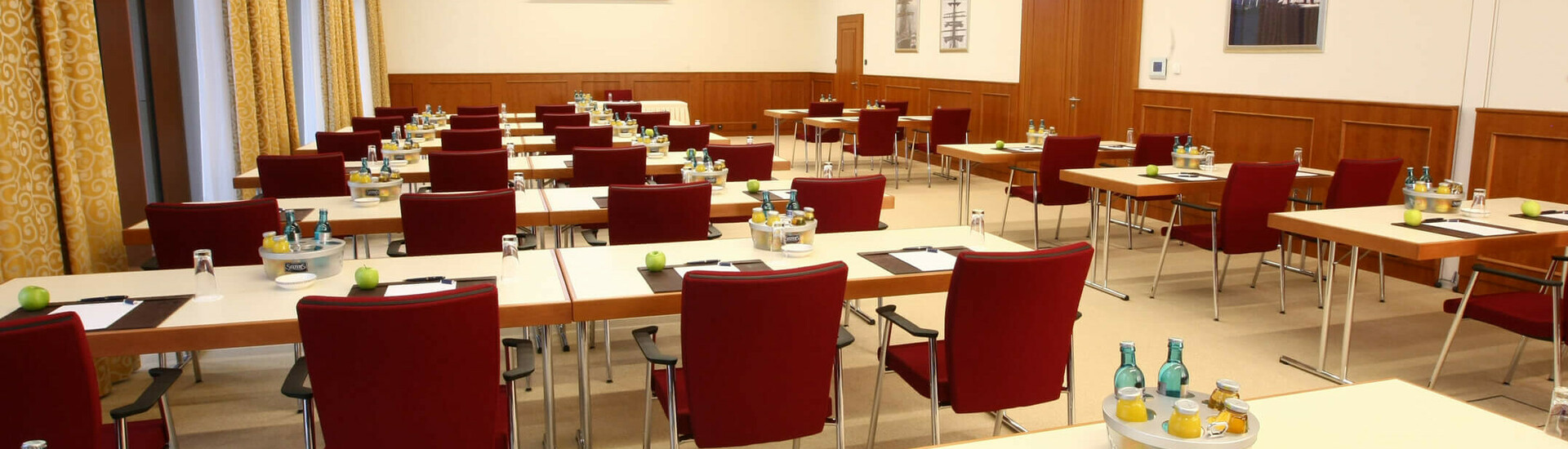Konferenzraum mit roten Stühlen, Tischen, Schreibmaterial und Getränken, ideal für Meetings im ATLANTIC Hotel Wilhelmshaven.