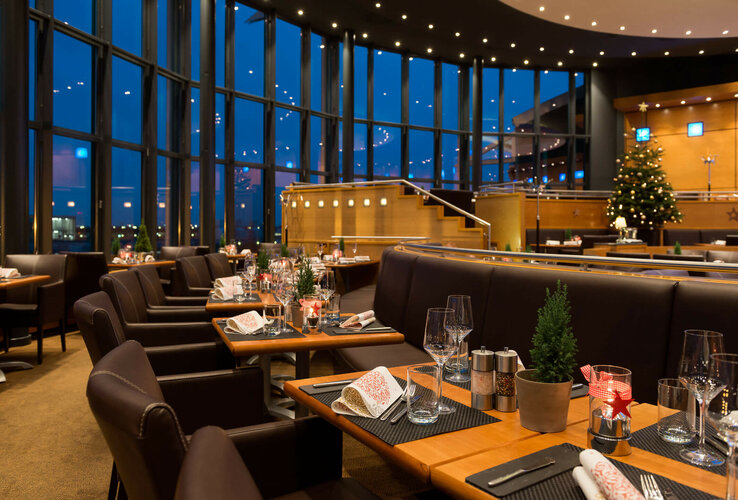 Modernes Restaurant im ATLANTIC Hotel Airport, Bremen, festlich gedeckt mit großen Fenstern und Weihnachtsbaum im Hintergrund.