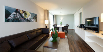 Bright hotel room with leather sofa, dining table, TV and horse picture on the wall at the ATLANTIC Hotel Galopprennbahn Bremen.