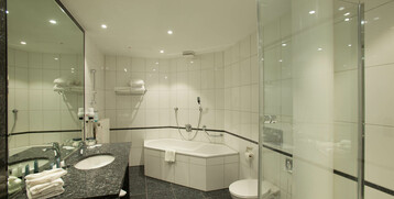 Modernes Hotelbad mit großer Badewanne, Dusche, Waschbecken und WC, elegant gefliest in Weiß und Schwarz.