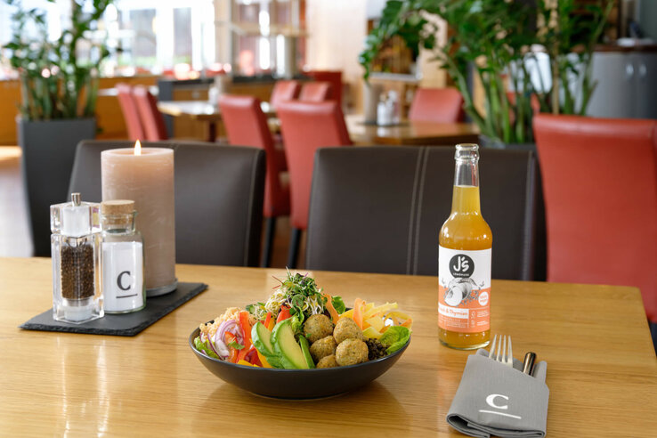 Ein gedeckter Tisch im ATLANTIC Hotel Universum mit Salat, Getränk und Kerze.