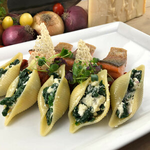 Gefüllte Muschelnudeln mit Spinat und Ricotta, garniert mit Lachs und Microgreens auf weißem Teller.