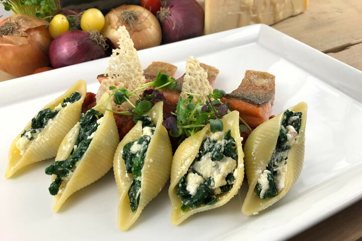 Stuffed shell pasta with spinach and ricotta, garnished with salmon and microgreens on a white plate.