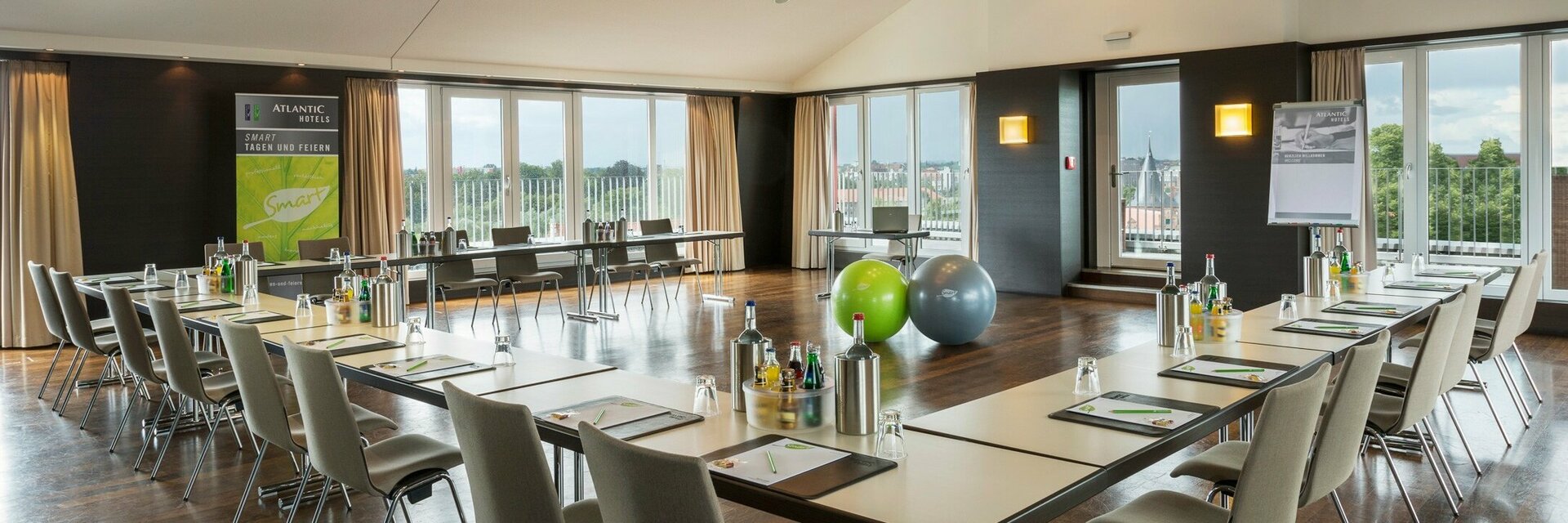 Moderner Konferenzraum mit U-förmiger Tischanordnung, Stühlen, Flipchart und großen Fenstern mit Blick ins Grüne.