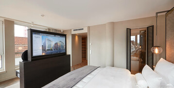 Modern hotel room with large bed, flat-screen TV, stylish lighting and view of a terrace.