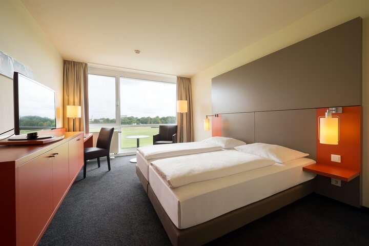 Modern ausgestattete Doppelzimmer mit Blick auf die die Rennbahn Modernes Hotelzimmer mit Doppelbett, Schreibtisch, TV und großem Fenster mit Blick auf die Galopprennbahn.