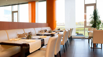 Modern restaurant with white seating, laid tables and a view of the racecourse through large windows.