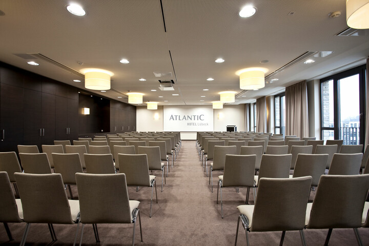 Modern conference room in the ATLANTIC Hotel Lübeck with rows of chairs, stage and large windows.