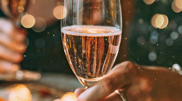 Zwei Menschen halten Champagnergläser in festlicher Dekoration.