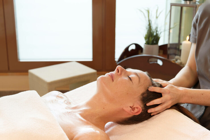Person enjoying a head massage in a spa, surrounded by candles and plants, lying on a massage table.