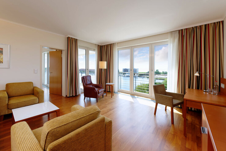 Helles Hotelzimmer mit Sitzbereich, Schreibtisch und großem Fenster mit Blick auf den Hafen.