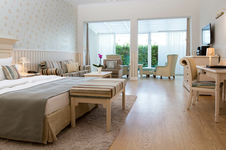 Helles Hotelzimmer mit Doppelbett, gemütlicher Sitzecke, Schreibtisch und großem Fenster mit Blick ins Grüne.