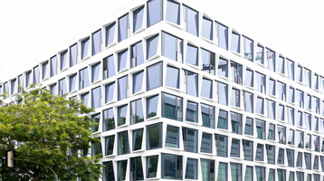 Facade with honeycomb structure l ATLANTIC Hotel Münster Modern hotel building with geometric glass façade and green tree in the foreground.