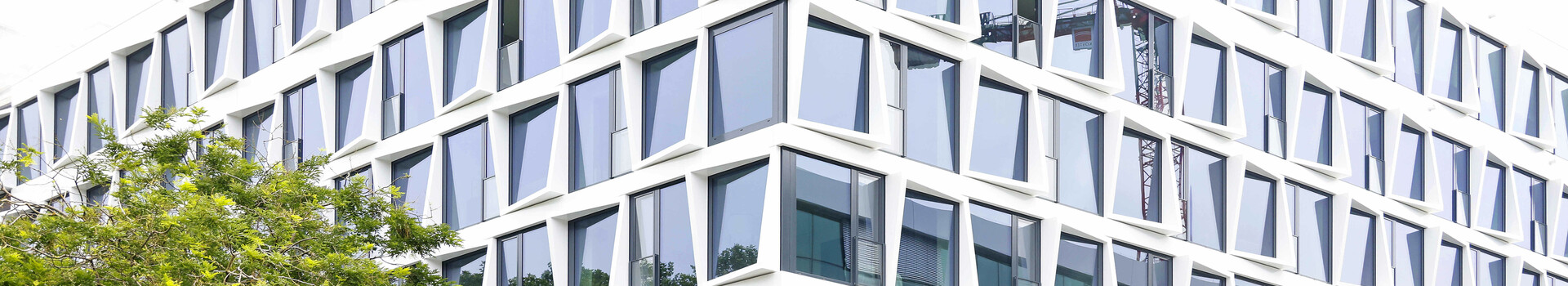Modernes Hotelgebäude mit geometrischer Glasfassade und grünem Baum im Vordergrund.