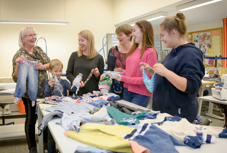 Group of people laughing and looking at colorful fabrics in a bright room.