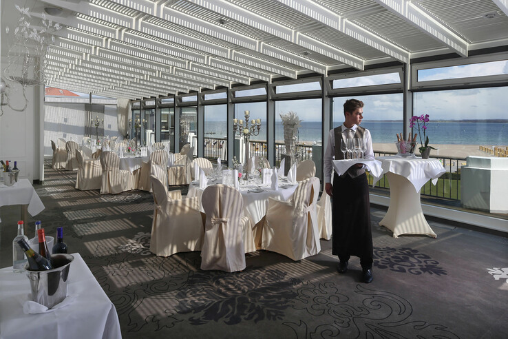 Heller Speisesaal mit Meerblick, gedeckten Tischen und Kellner im ATLANTIC Grand Hotel Travemünde.