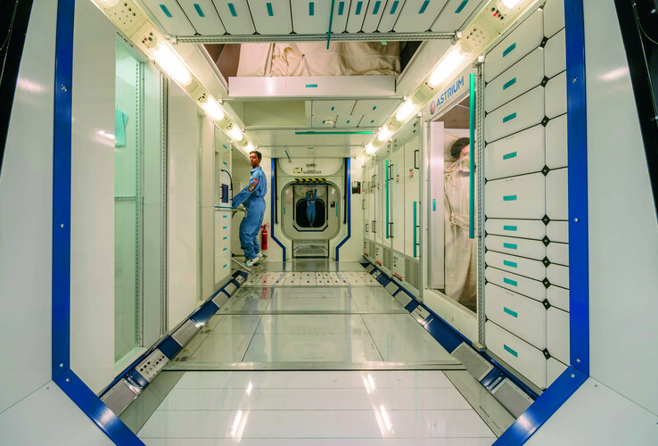 Modern room with futuristic design, blue accents and a man in a blue uniform in a brightly lit corridor.